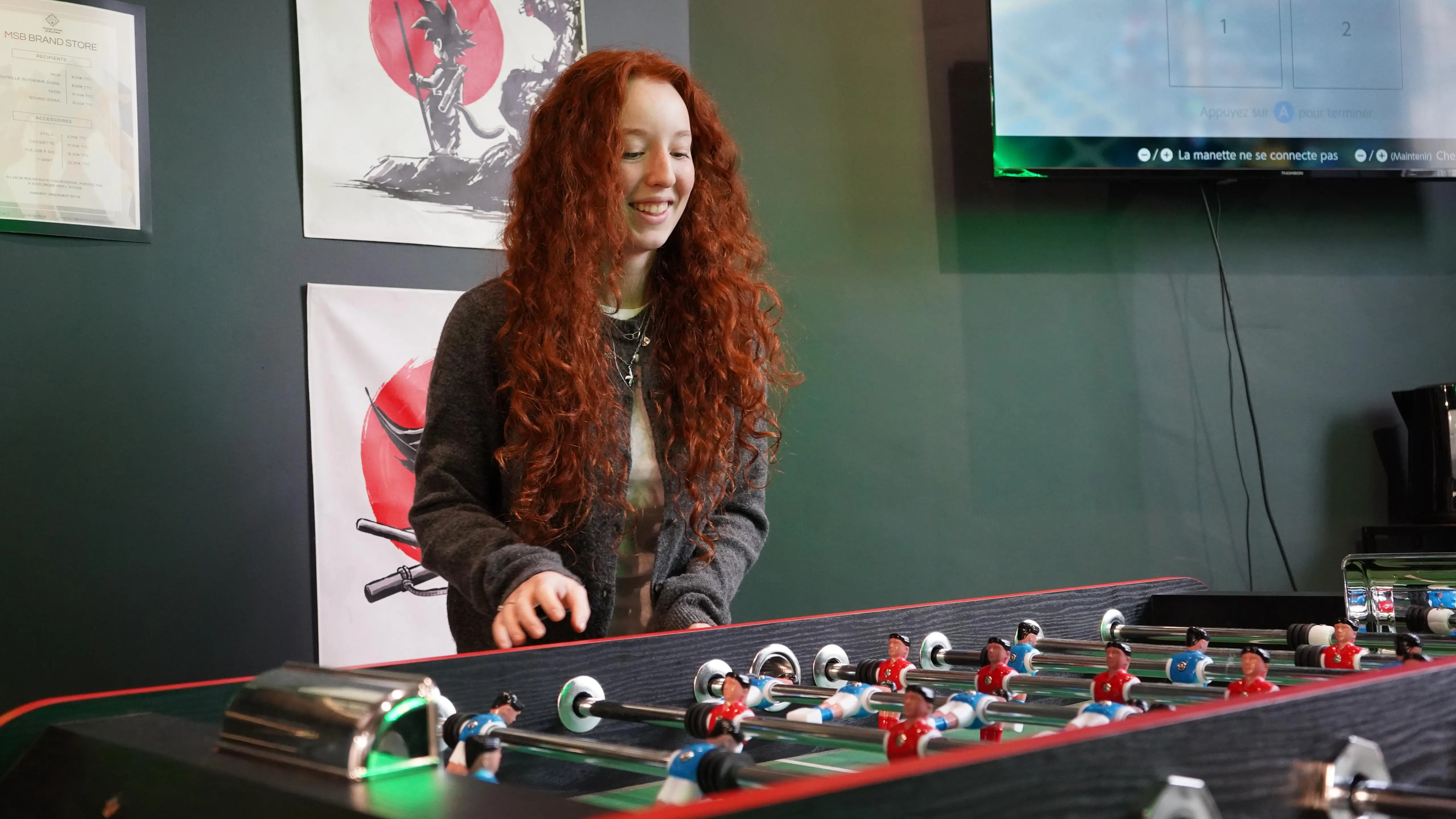 Étudiante souriante en pleine partie de babyfoot dans l'espace détente