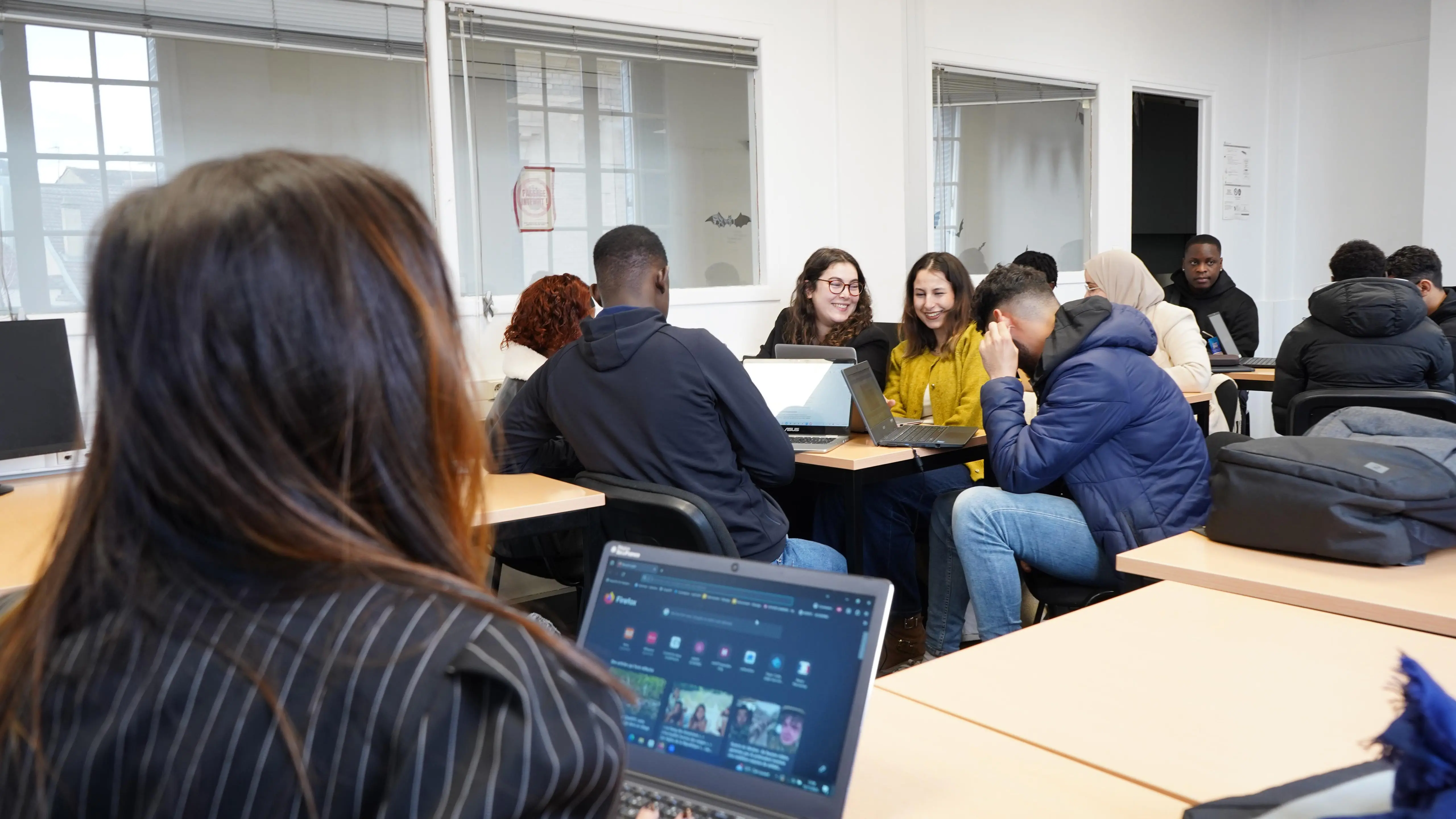 Groupe d'étudiants au travail sur ordinateurs en salle de cours, sourires échangés