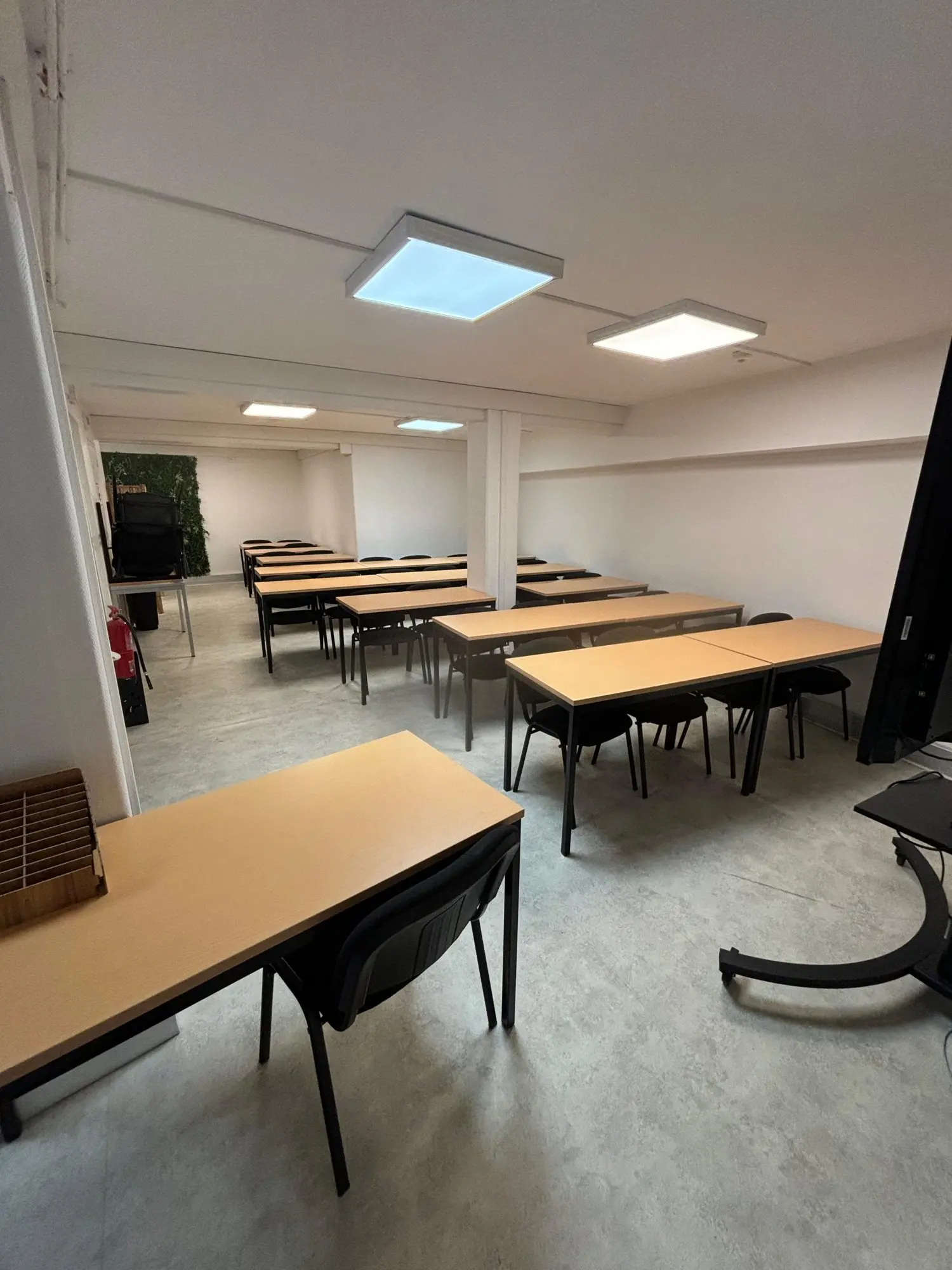 Salle de cours lumineuse avec tables en bois clair et écran